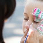 Little girl getting her face painted by face painting artist.